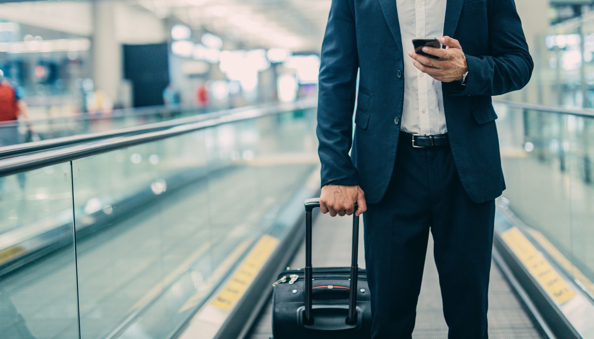 Businessman walking with luggage and using mobile phone at airport